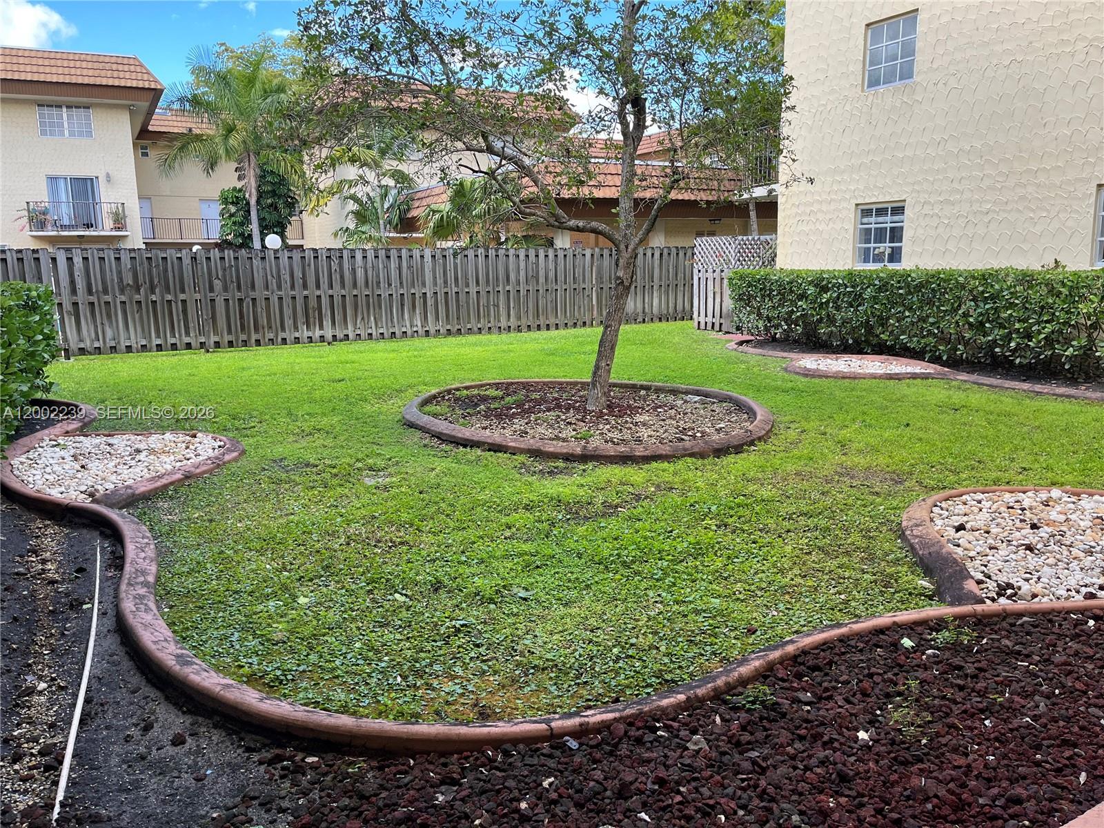 A grassy backyard features a central tree, stone-bordered garden beds, and a wooden privacy fence — 8650 SW 109th Ave # 111, Miami FL 33173, MIAMI, FL