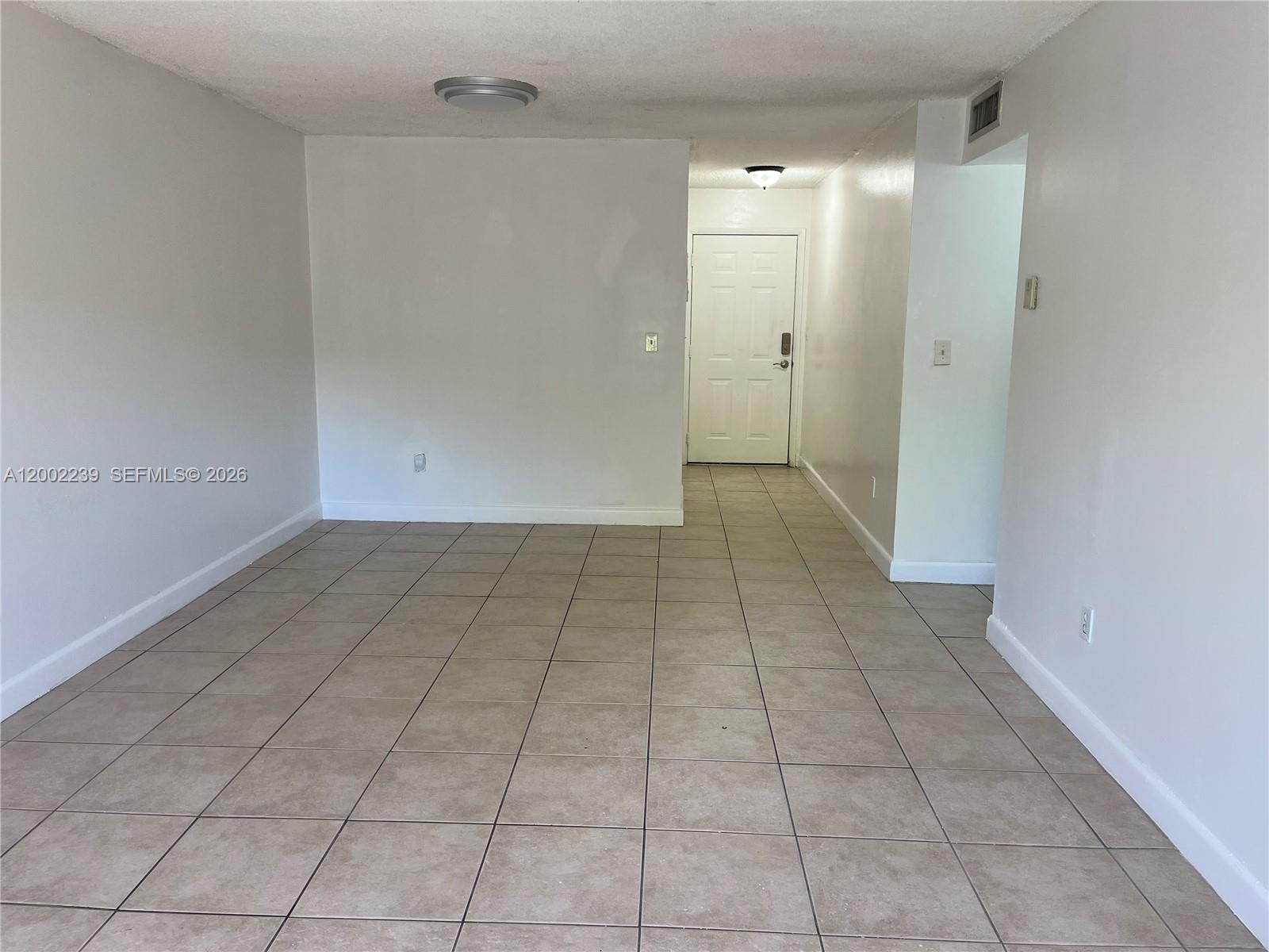A room with light-colored walls and beige tile flooring leads to an entryway door — 8650 SW 109th Ave # 111, Miami FL 33173, MIAMI, FL