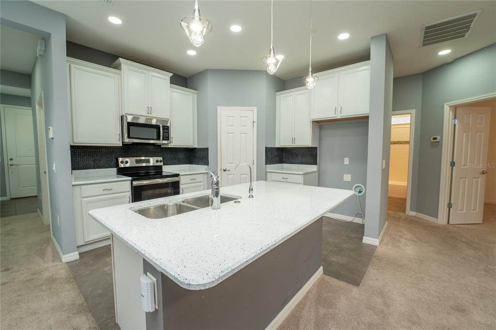 A kitchen with white cabinets, a quartz-topped island, and dark tile flooring — 157 PALAZZO LANE, KISSIMMEE, FL