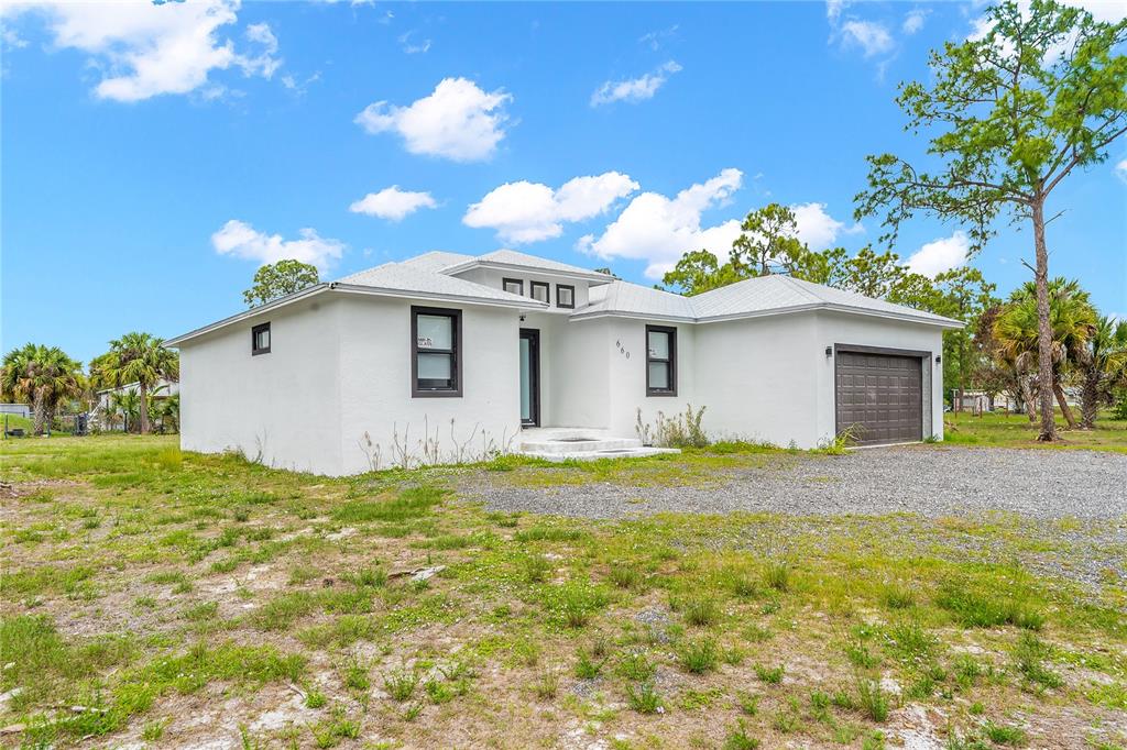 A white, single-story house with a gravel driveway and a dark-colored garage door — 660 S ZAMBRIA STREET, CLEWISTON, FL