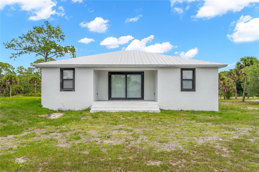 The exterior of a white, single-story house features a metal roof and black-framed windows — 660 S ZAMBRIA STREET, CLEWISTON, FL