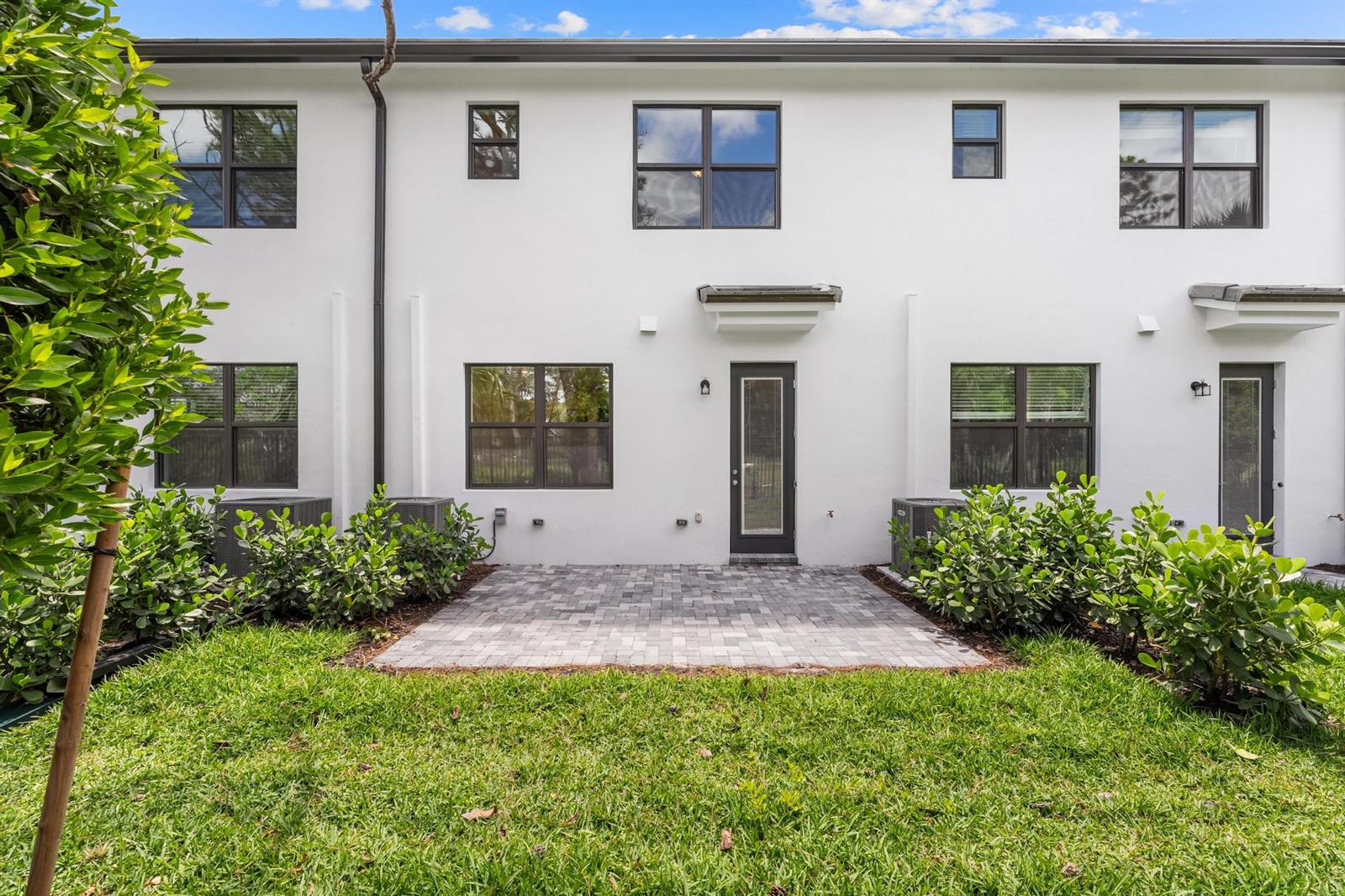 The exterior rear view of a white two-story townhouse features a paved patio and landscaping — 4315 Efendi Drive, Lantana FL 33462, LANTANA, FL