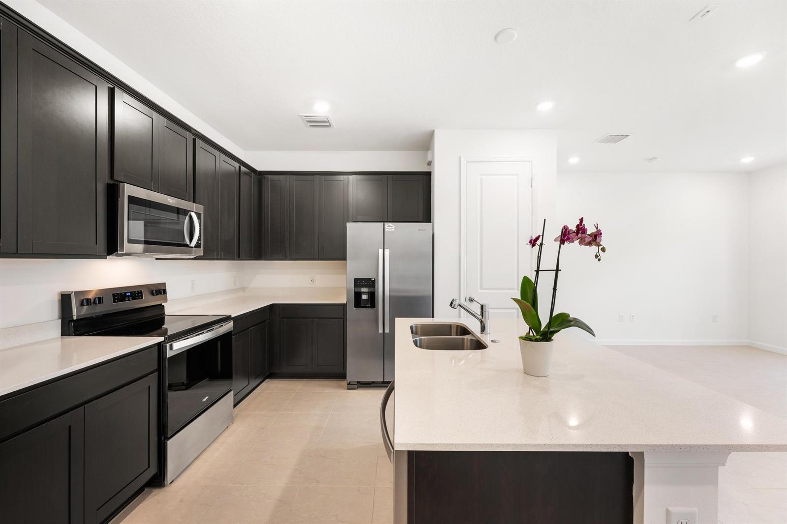 A kitchen features dark cabinets, stainless steel appliances, a quartz island, and light tile flooring — 4315 Efendi Drive, Lantana FL 33462, LANTANA, FL