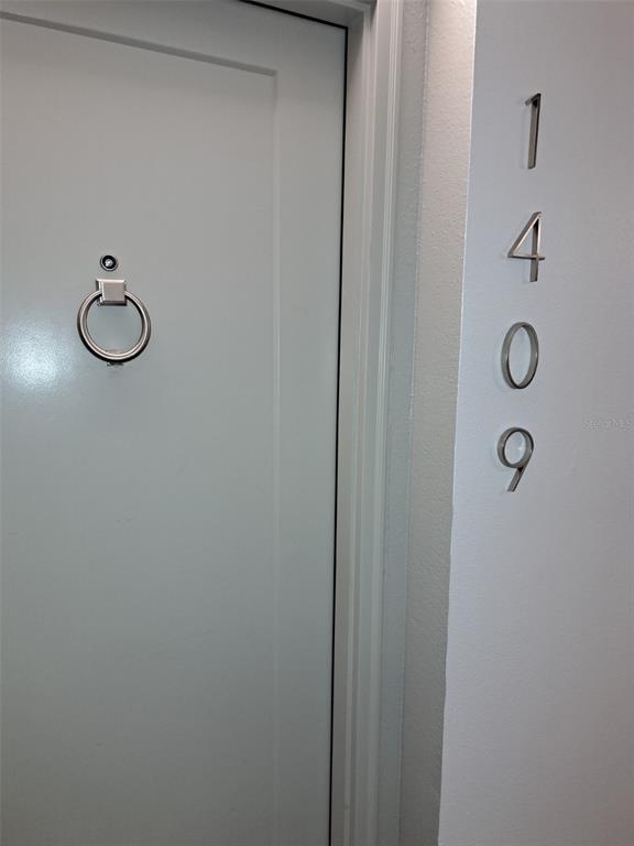 A white door with a silver knocker and peephole is labeled with the number 1409 — 400 ISLAND WAY UNIT 1409, CLEARWATER BEACH, FL