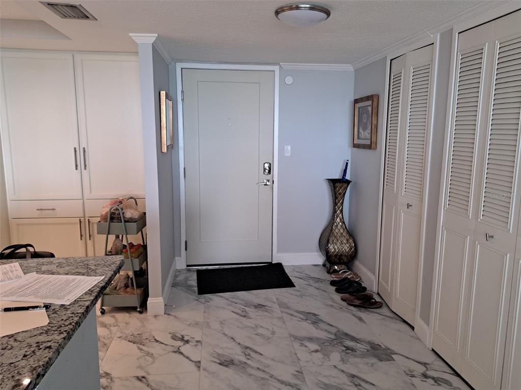 An entryway features marble-patterned tile flooring, a light-colored front door, and white louvered closet doors — 400 ISLAND WAY UNIT 1409, CLEARWATER BEACH, FL