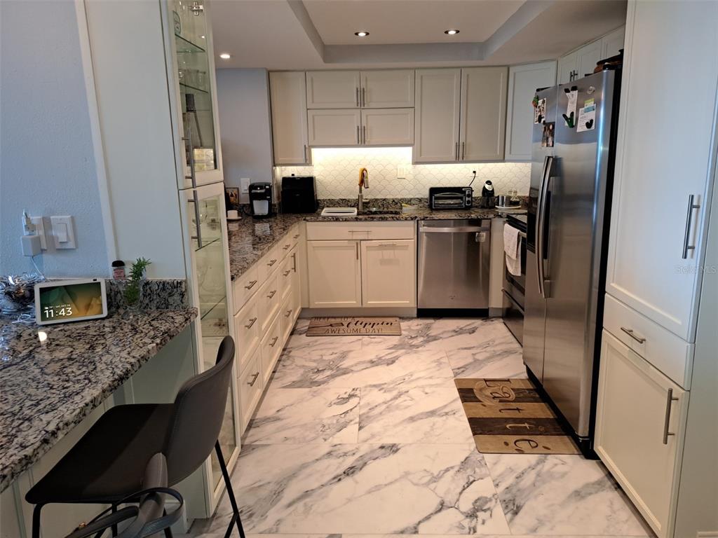 A kitchen features white cabinets, granite countertops, stainless steel appliances, and marble-patterned tile flooring — 400 ISLAND WAY UNIT 1409, CLEARWATER BEACH, FL