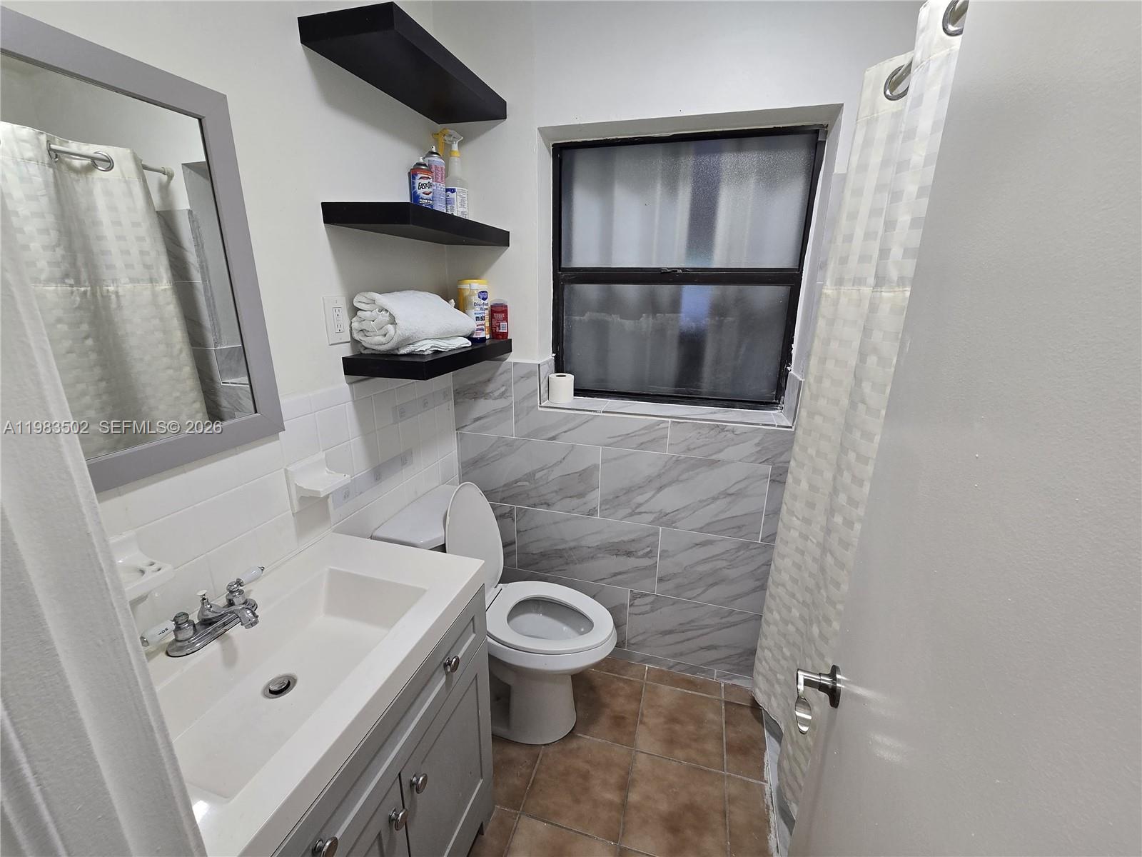 A bathroom features a gray vanity, a toilet, floating shelves, and a tiled shower area — 704 SW 2nd Ave, Dania Beach FL 33004, DANIA BEACH, FL