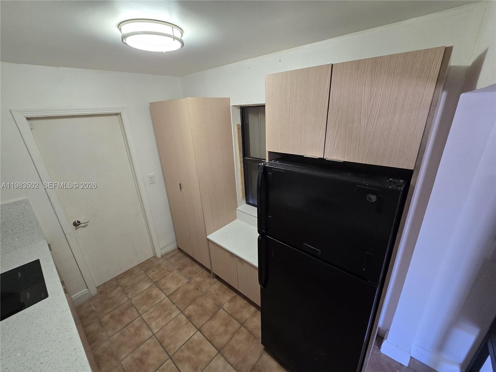 A kitchen features light wood cabinets, a black refrigerator, and tan tile flooring — 704 SW 2nd Ave, Dania Beach FL 33004, DANIA BEACH, FL