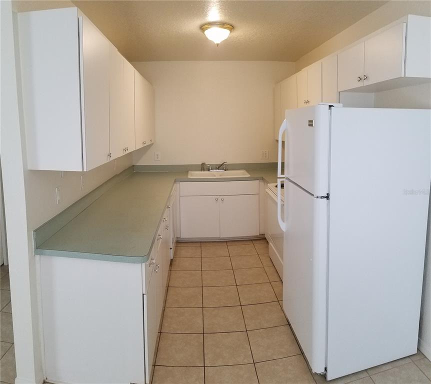 A galley kitchen features white cabinets, green laminate countertops, a white refrigerator, and tiled flooring — 1673 SW 107TH LANE, OCALA, FL
