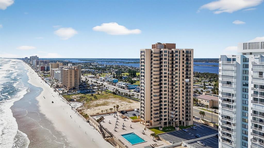 An aerial view shows a tall beachfront condominium building with a pool and parking lot — 3051 S ATLANTIC AVENUE UNIT 1005, DAYTONA BEACH SHORES, FL