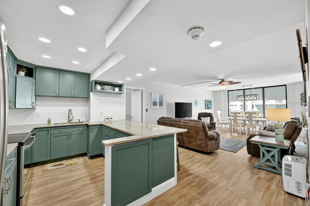 An open-concept kitchen with teal cabinets and a breakfast bar overlooks a living and dining area — 3051 S ATLANTIC AVENUE UNIT 1005, DAYTONA BEACH SHORES, FL