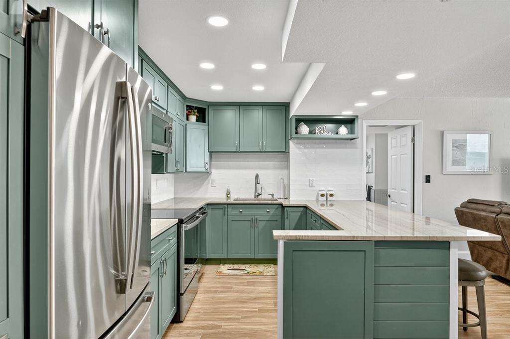 A kitchen features teal cabinets, stainless steel appliances, and a white countertop peninsula — 3051 S ATLANTIC AVENUE UNIT 1005, DAYTONA BEACH SHORES, FL