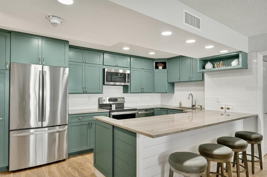 A kitchen features teal cabinets, stainless steel appliances, a breakfast bar, and light-colored countertops — 3051 S ATLANTIC AVENUE UNIT 1005, DAYTONA BEACH SHORES, FL
