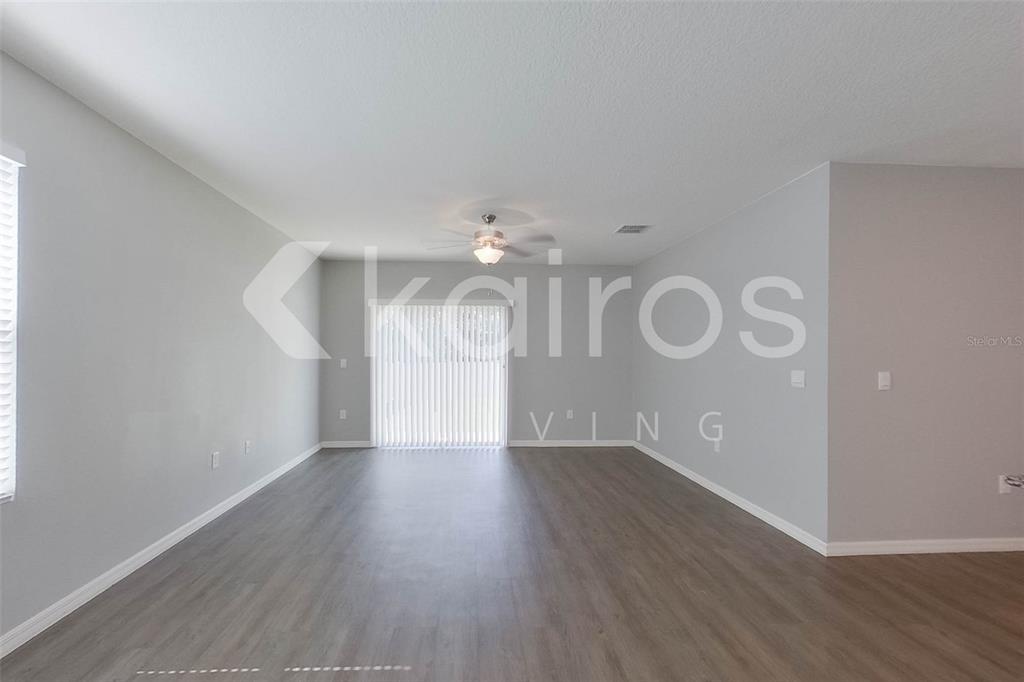 An empty living room features gray walls, wood-look flooring, and a sliding glass door — 31954 KATELIN CIRCLE, LEESBURG, FL