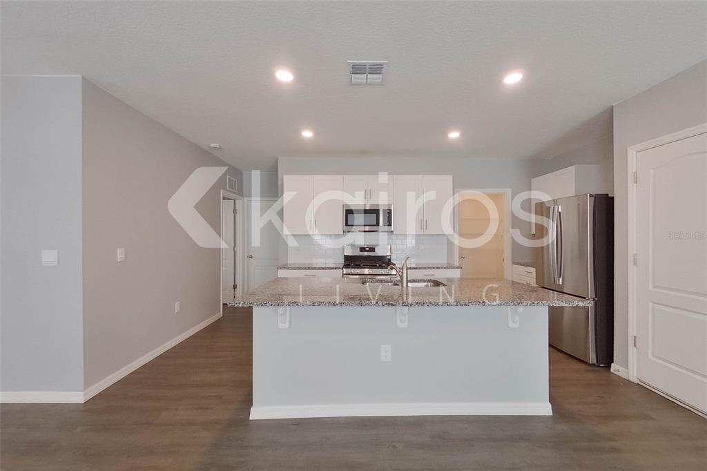A kitchen features a granite-topped island, stainless steel appliances, and white cabinetry — 31954 KATELIN CIRCLE, LEESBURG, FL