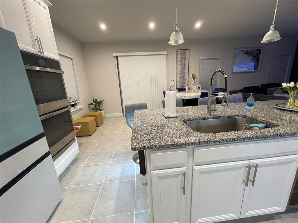 A kitchen features white cabinets, a granite-topped island with a sink, and tile flooring — 3182 ARMSTRONG SPRING DRIVE, KISSIMMEE, FL