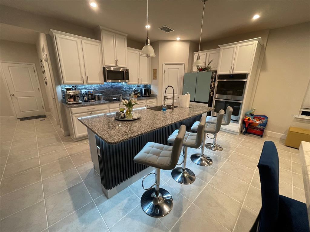 A kitchen features white cabinetry, granite countertops, a dark slatted island, and four bar stools — 3182 ARMSTRONG SPRING DRIVE, KISSIMMEE, FL