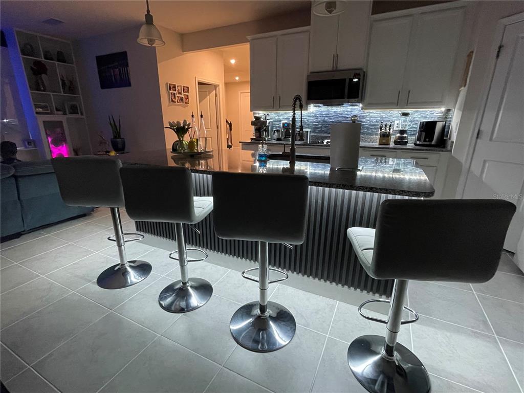 A kitchen features a dark-toned island with bar seating, white cabinetry, and tiled flooring — 3182 ARMSTRONG SPRING DRIVE, KISSIMMEE, FL