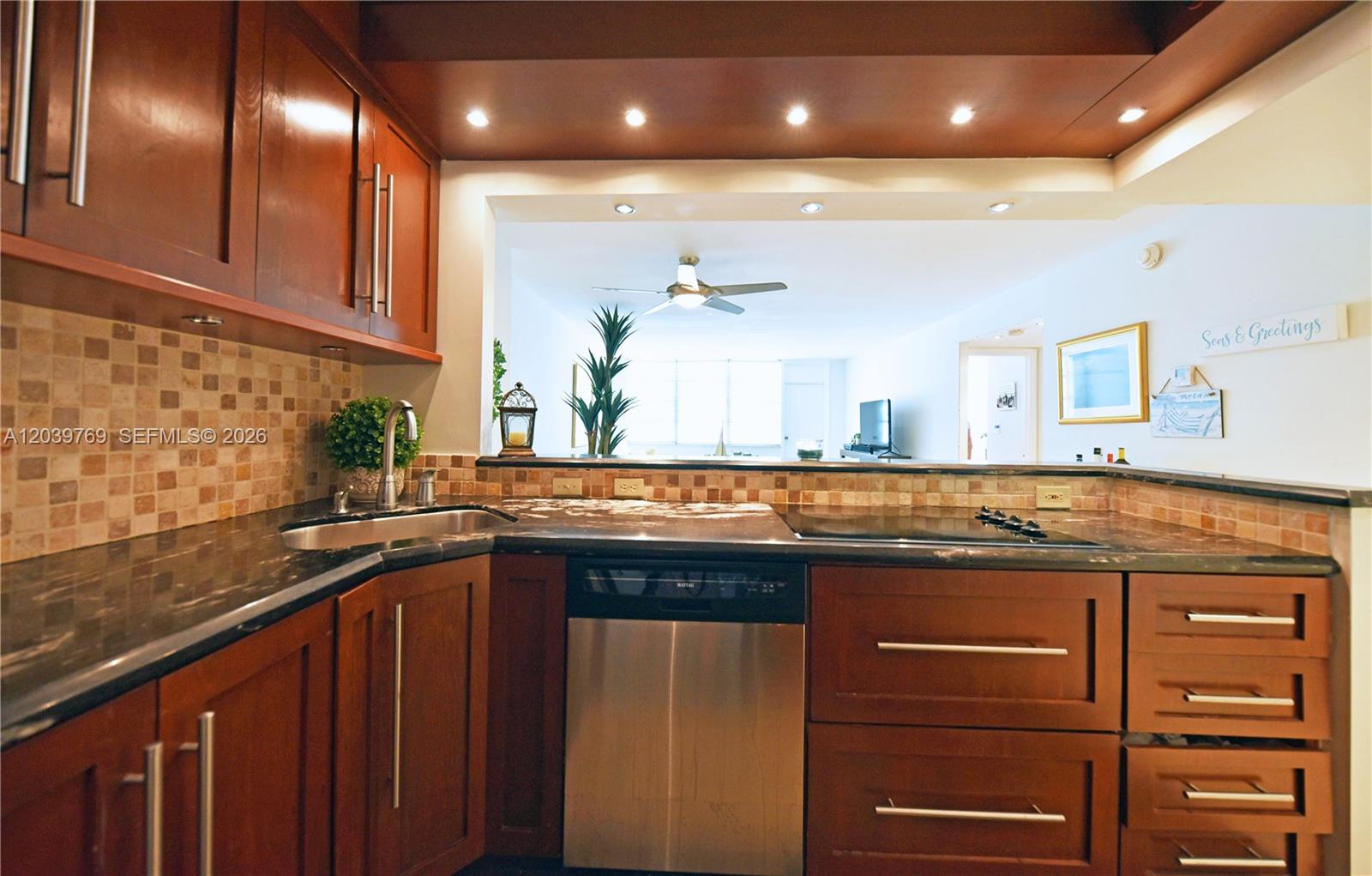 A kitchen features dark wood cabinets, granite countertops, a stainless steel dishwasher, and tiled backsplash — 2016 Bay Dr # 201, Miami Beach FL 33141, MIAMI BEACH, FL
