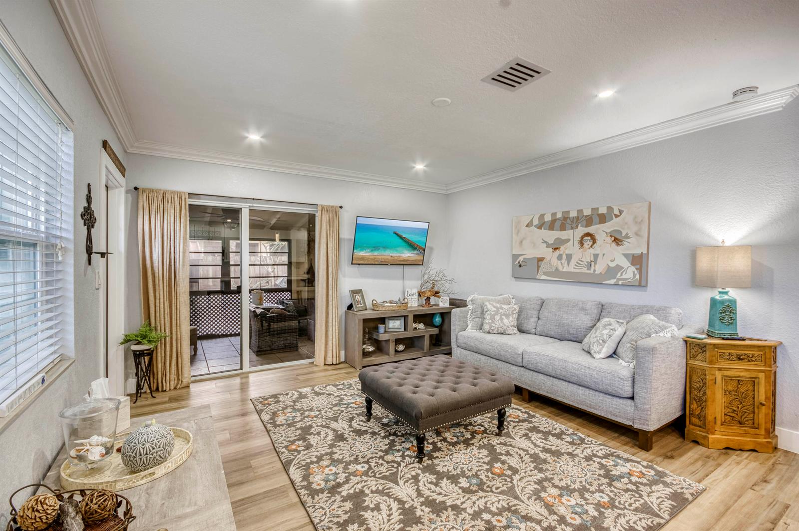 A living room features a gray sofa, tufted ottoman, patterned rug, and sliding glass doors — 404 S Caloosahatchee Avenue, Jupiter FL 33458, JUPITER, FL