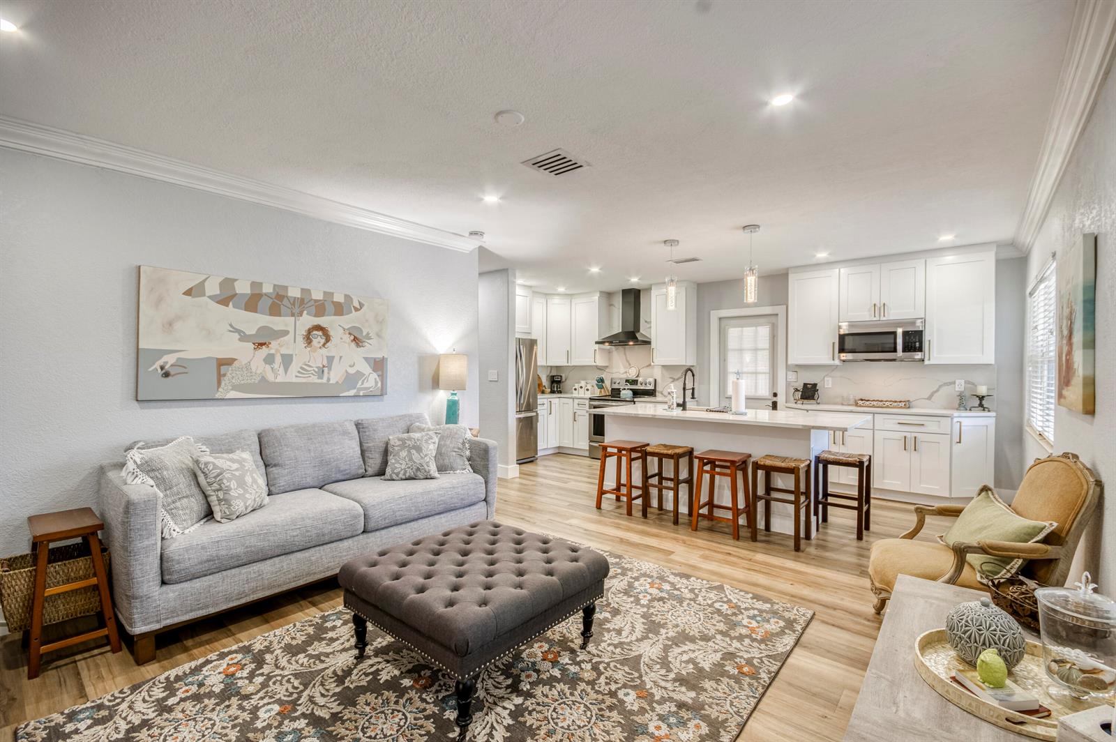 An open-concept living room and kitchen featuring a grey sofa, kitchen island, and white cabinetry — 404 S Caloosahatchee Avenue, Jupiter FL 33458, JUPITER, FL