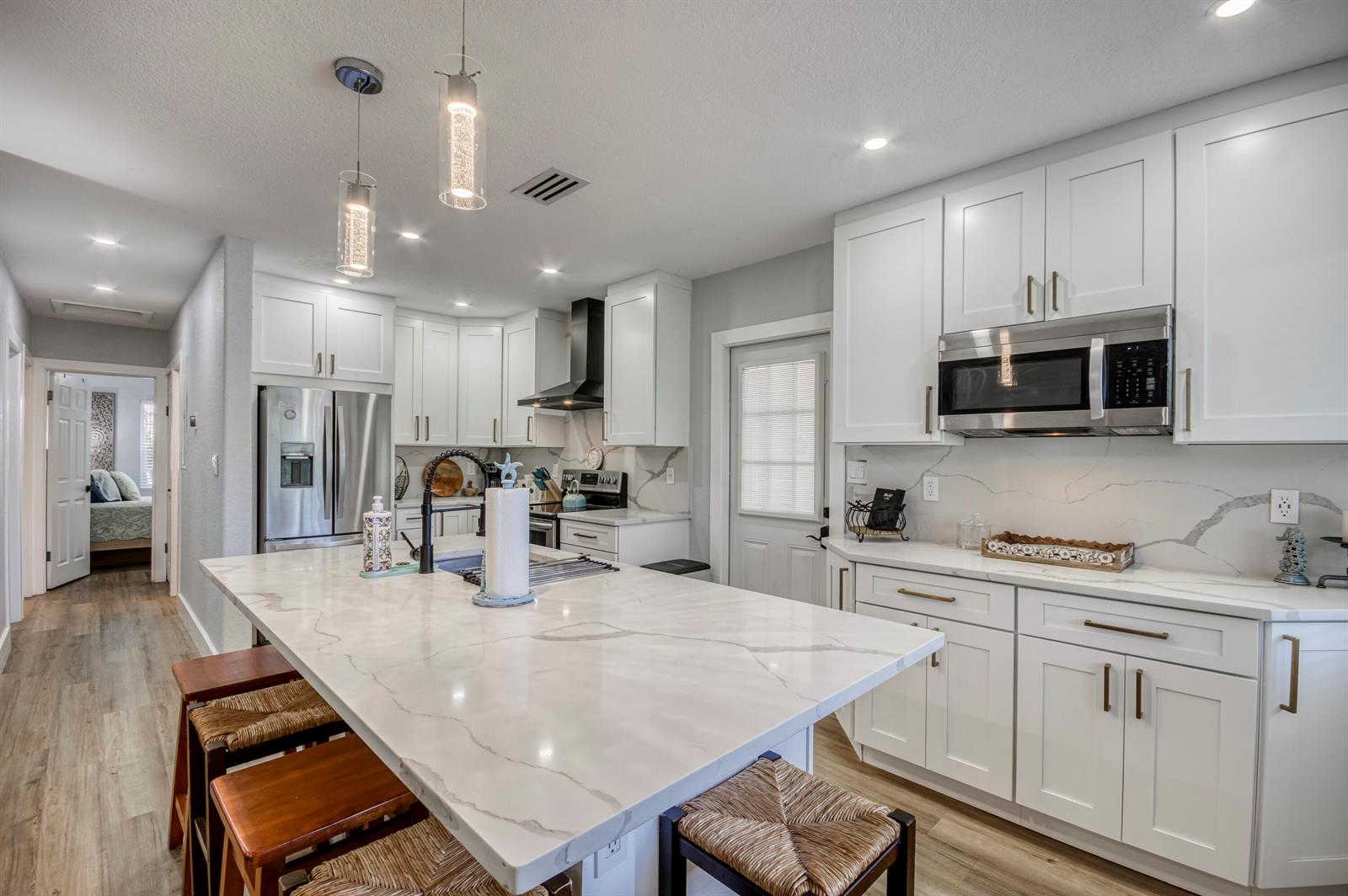 A modern kitchen features white cabinetry, a large marble-topped island, and stainless steel appliances — 404 S Caloosahatchee Avenue, Jupiter FL 33458, JUPITER, FL