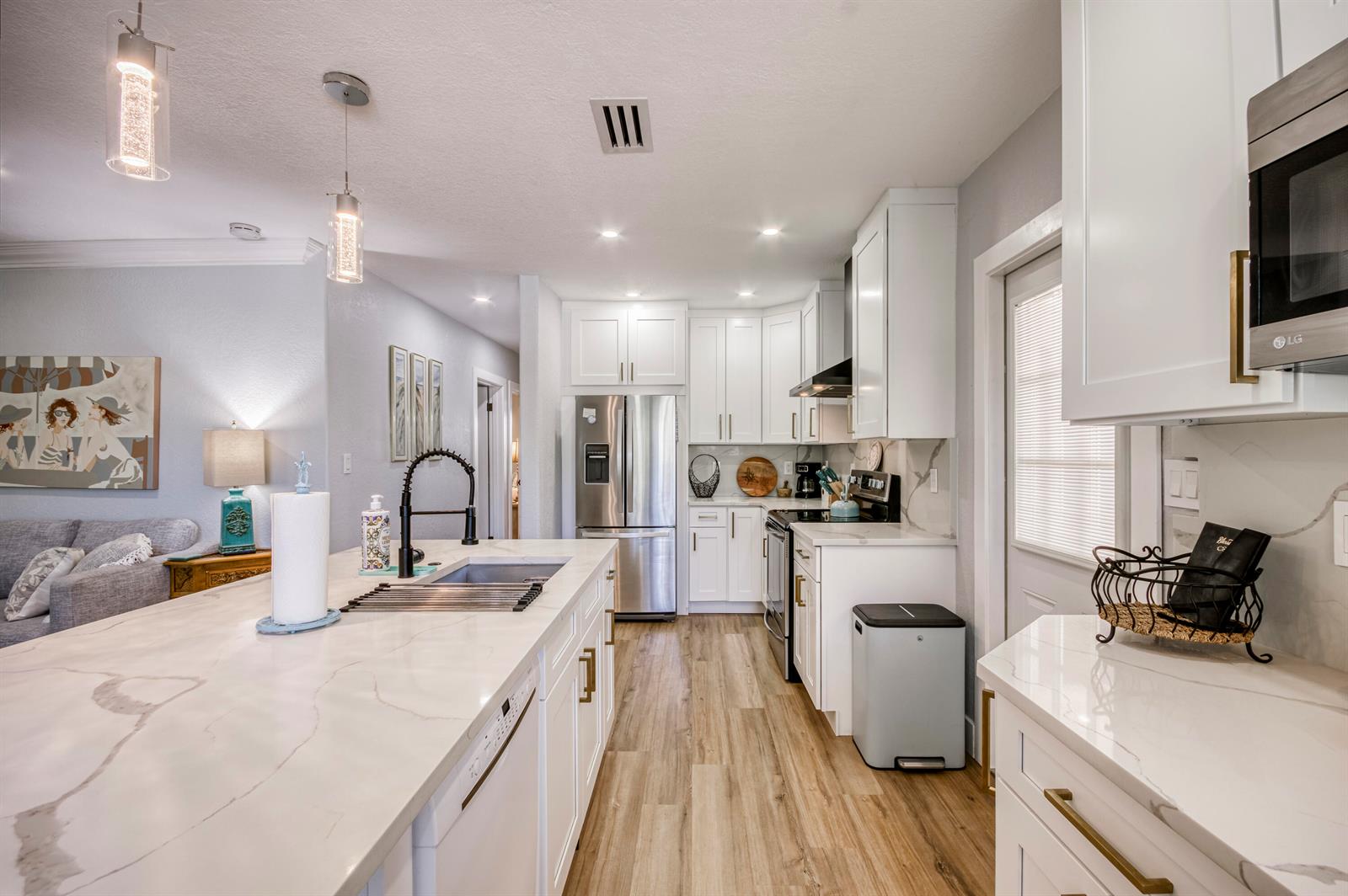 A modern kitchen features white cabinetry, marble countertops, stainless steel appliances, and wood-look flooring — 404 S Caloosahatchee Avenue, Jupiter FL 33458, JUPITER, FL