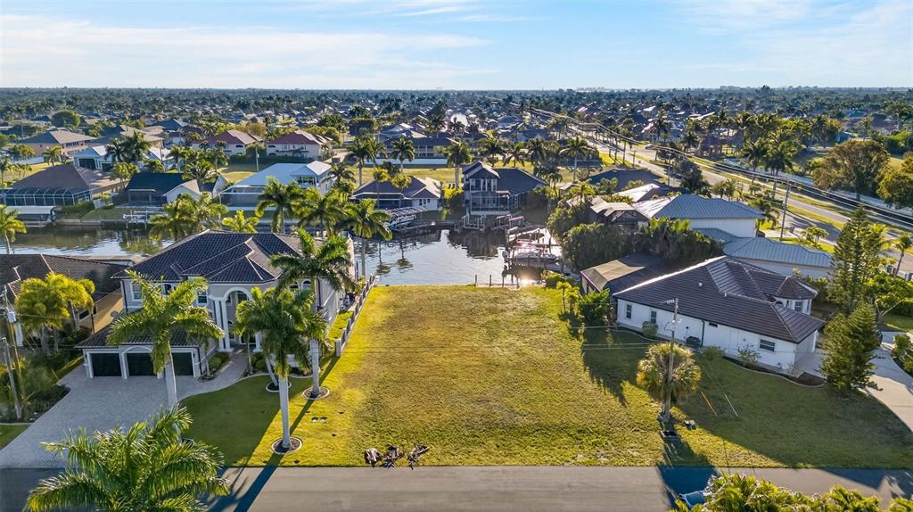 An aerial view shows a vacant waterfront lot situated between two large residential homes — 5423 SW 17TH AVENUE, CAPE CORAL, FL