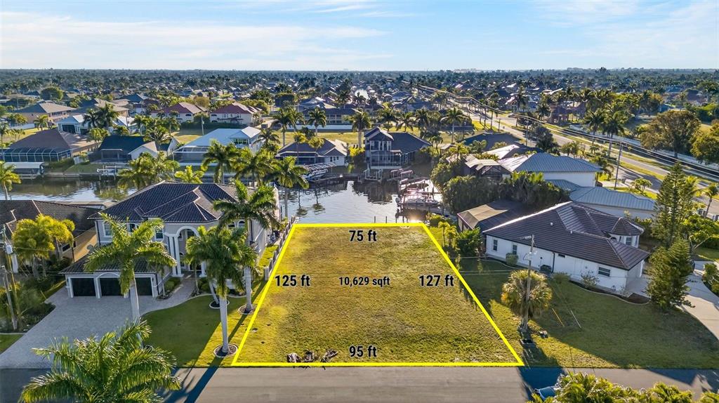 An aerial view shows a vacant waterfront residential lot outlined in yellow — 5423 SW 17TH AVENUE, CAPE CORAL, FL
