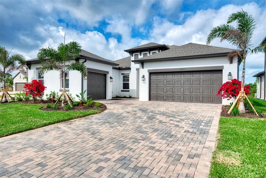 A single-story house with a paved driveway, two garage doors, and palm trees — 5825 MILLENNIUM SILVER COURT, SARASOTA, FL