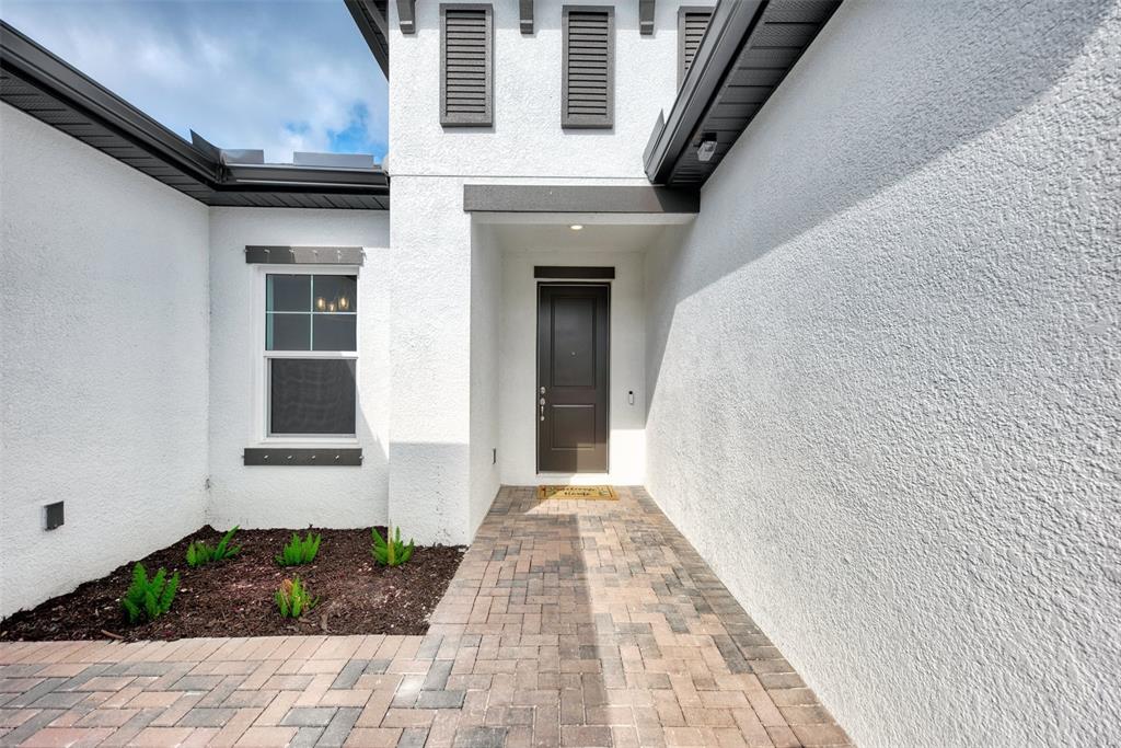 A paved walkway leads to the dark front door of a white stucco house — 5825 MILLENNIUM SILVER COURT, SARASOTA, FL