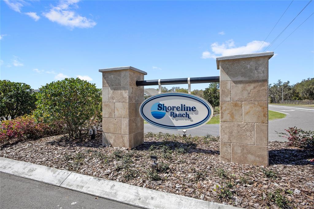 A stone monument sign for Shoreline Ranch stands beside a road under a blue sky — 20280 SHORELINE RANCH LANE, UMATILLA, FL
