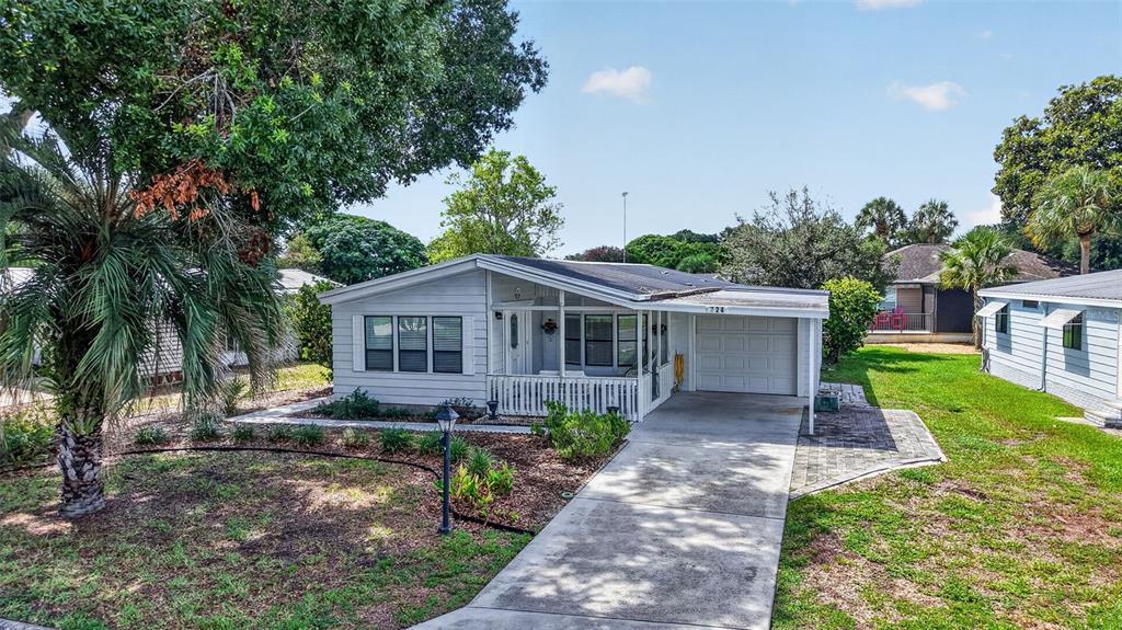 A single-story light gray house with a front porch, attached garage, and concrete driveway — 724 JASON DRIVE, THE VILLAGES, FL