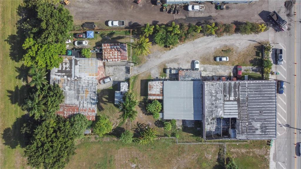 An aerial view shows two commercial buildings with metal roofs surrounded by trees and parking — 185 E MAIN STREET, PAHOKEE, FL