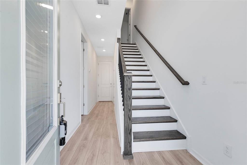 A bright entryway features light wood-look flooring, white walls, and a staircase with dark treads — 8472 SPERRY STREET, ORLANDO, FL