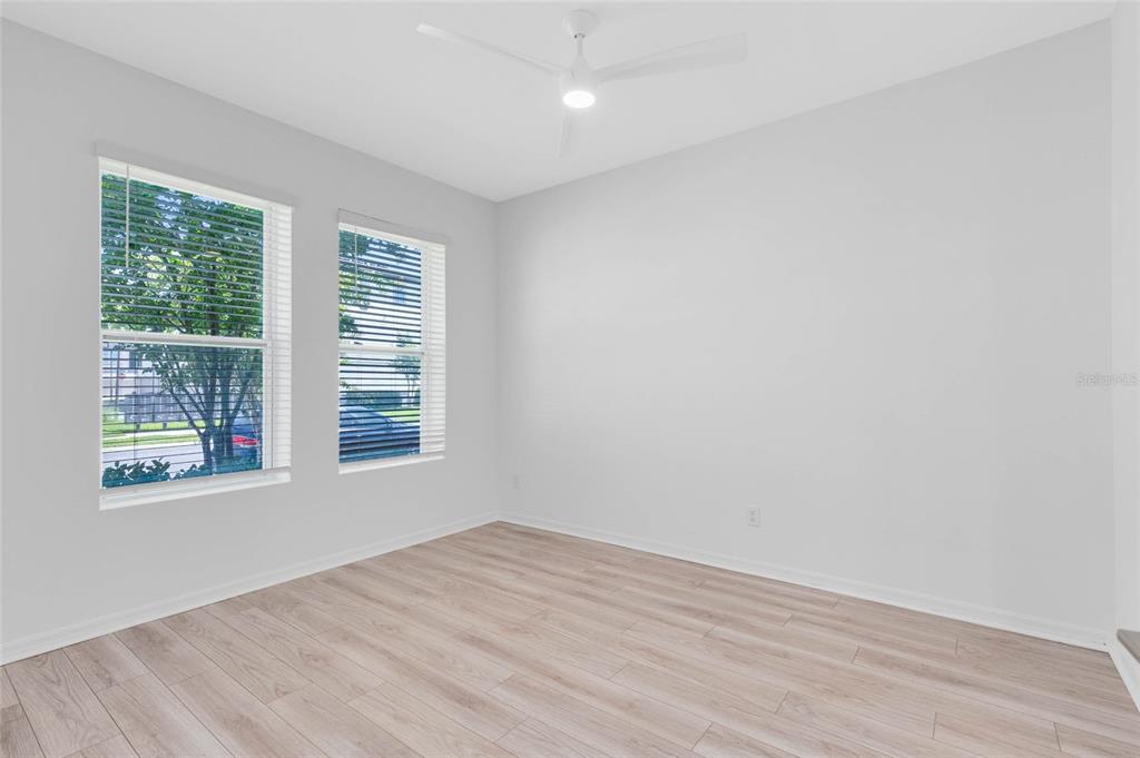 An empty bedroom features light wood-look flooring, white walls, and two windows with blinds — 8472 SPERRY STREET, ORLANDO, FL