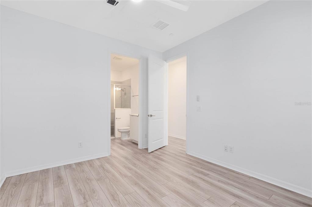 A bedroom with light wood-look flooring, white walls, and an attached bathroom — 8472 SPERRY STREET, ORLANDO, FL