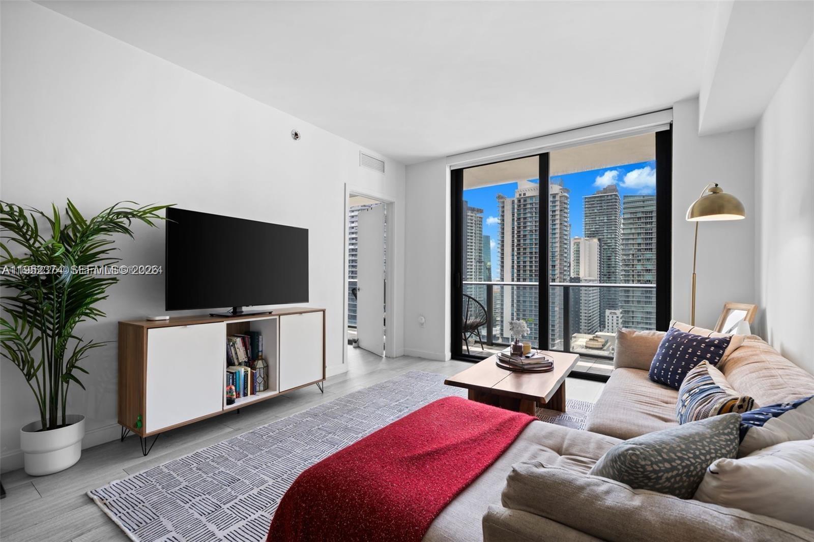 A modern living room features a television, sectional sofa, and floor-to-ceiling windows with city views — 55 SW 9th St # 2305, Miami FL 33130, MIAMI, FL