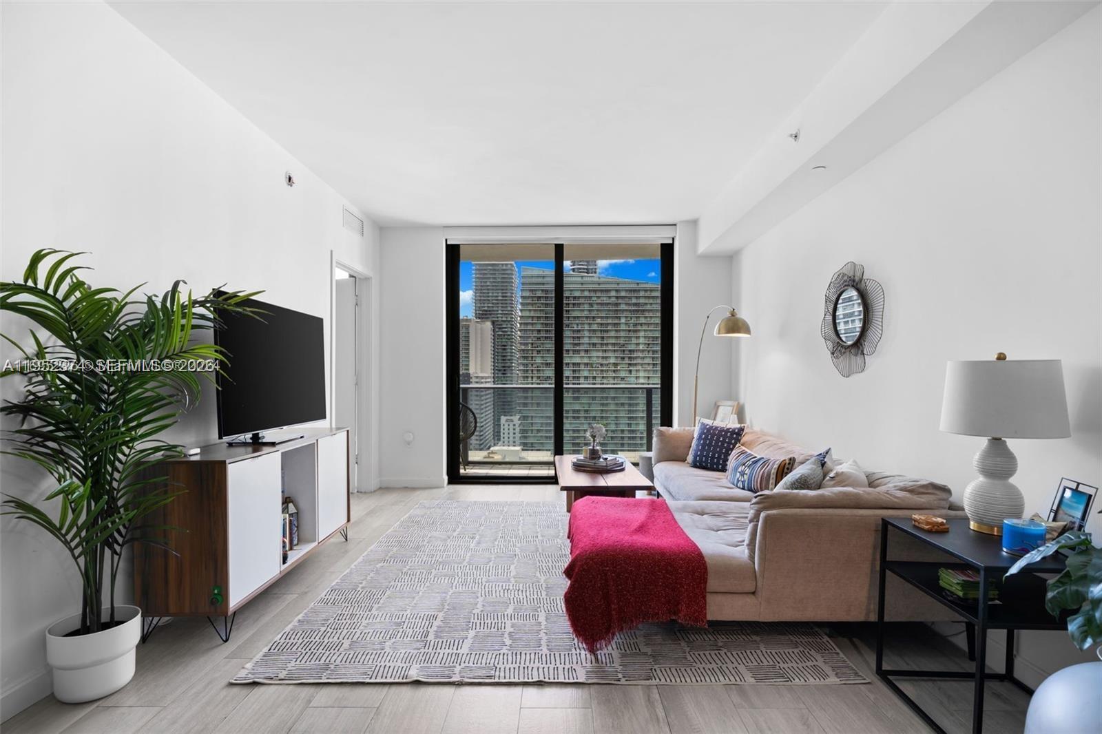 A living room features a beige sofa, a television on a console, and a balcony view — 55 SW 9th St # 2305, Miami FL 33130, MIAMI, FL