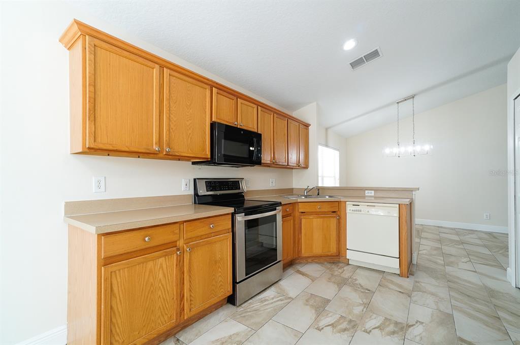 A kitchen features oak cabinets, stainless steel appliances, a white dishwasher, and light-colored tile flooring — 13518 BRIARMOOR COURT, ORLANDO, FL