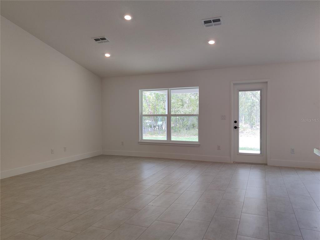 A bright, empty room features white walls, tile flooring, recessed lighting, a large window, and a glass-paned door — 15406 SCAUP DUCK AVENUE, WEEKI WACHEE, FL