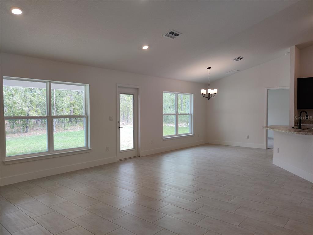 An open-concept living area features light tile flooring, white walls, large windows, and a chandelier — 15406 SCAUP DUCK AVENUE, WEEKI WACHEE, FL