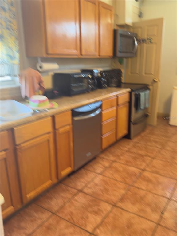 A kitchen features wood cabinets, tile flooring, a dishwasher, and a microwave above the stove — 1275 N BANANA RIVER DRIVE, MERRITT ISLAND, FL