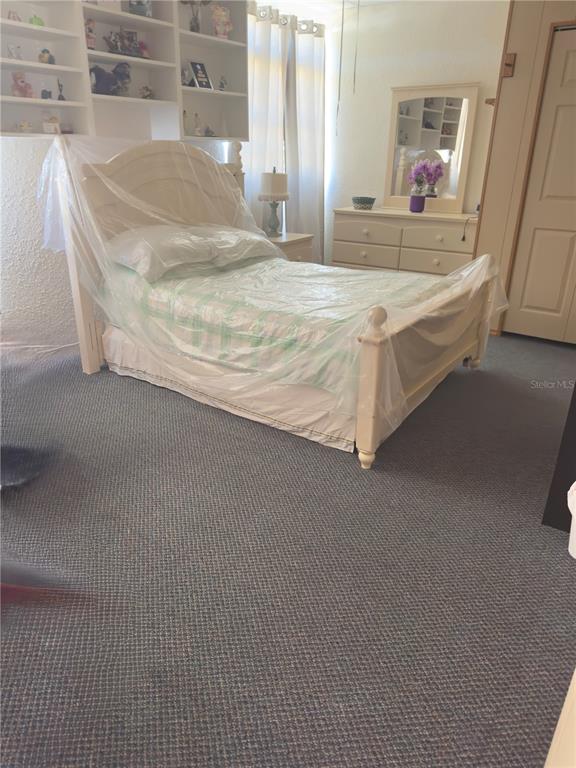 A bedroom features a bed covered in plastic, built-in shelving, a dresser, and blue carpeting — 1275 N BANANA RIVER DRIVE, MERRITT ISLAND, FL