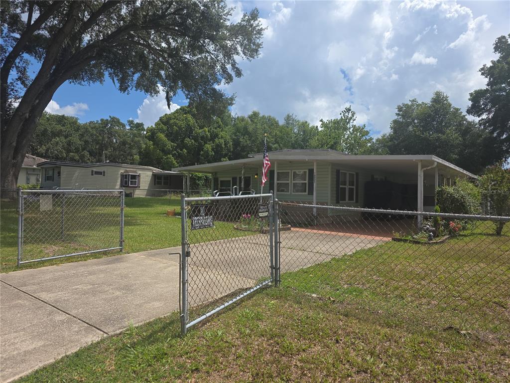 A single-story house with a carport and chain-link fence sits on a grassy lot — 16920 SE 101ST AVENUE ROAD, SUMMERFIELD, FL