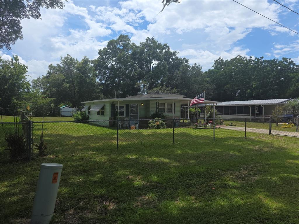 A single-story house with a light green exterior sits behind a chain-link fence — 16920 SE 101ST AVENUE ROAD, SUMMERFIELD, FL
