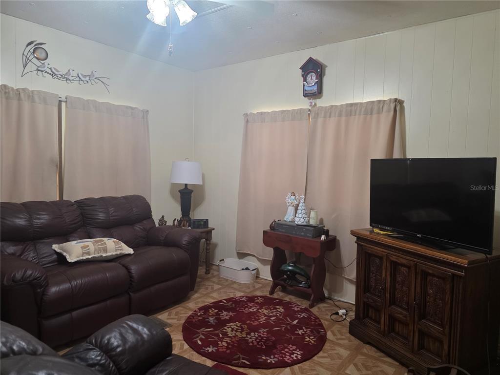 A living room features brown leather sofas, a television on a wooden cabinet, and curtains — 16920 SE 101ST AVENUE ROAD, SUMMERFIELD, FL