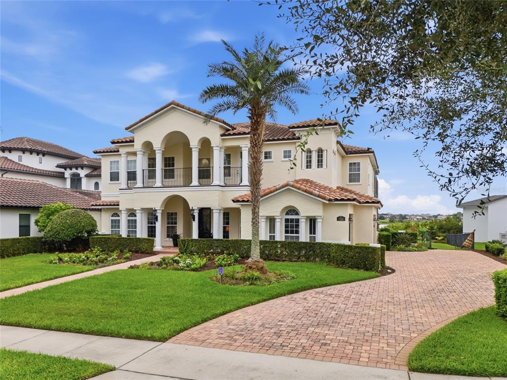 A two-story Mediterranean-style house with a tile roof, arched balconies, and a brick paver driveway — 7301 WILD BLACKBERRY TRAIL, WINTER GARDEN, FL