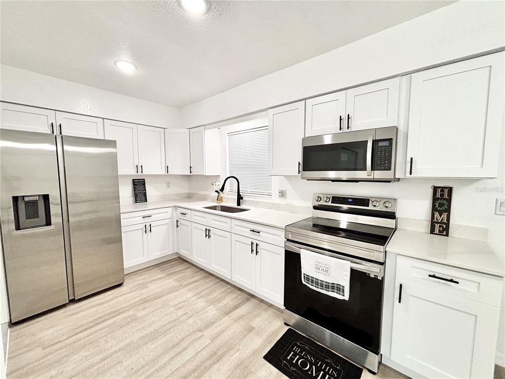 A kitchen features white cabinets, stainless steel appliances, and light wood-look flooring — 1516 AVENUE D NE, WINTER HAVEN, FL