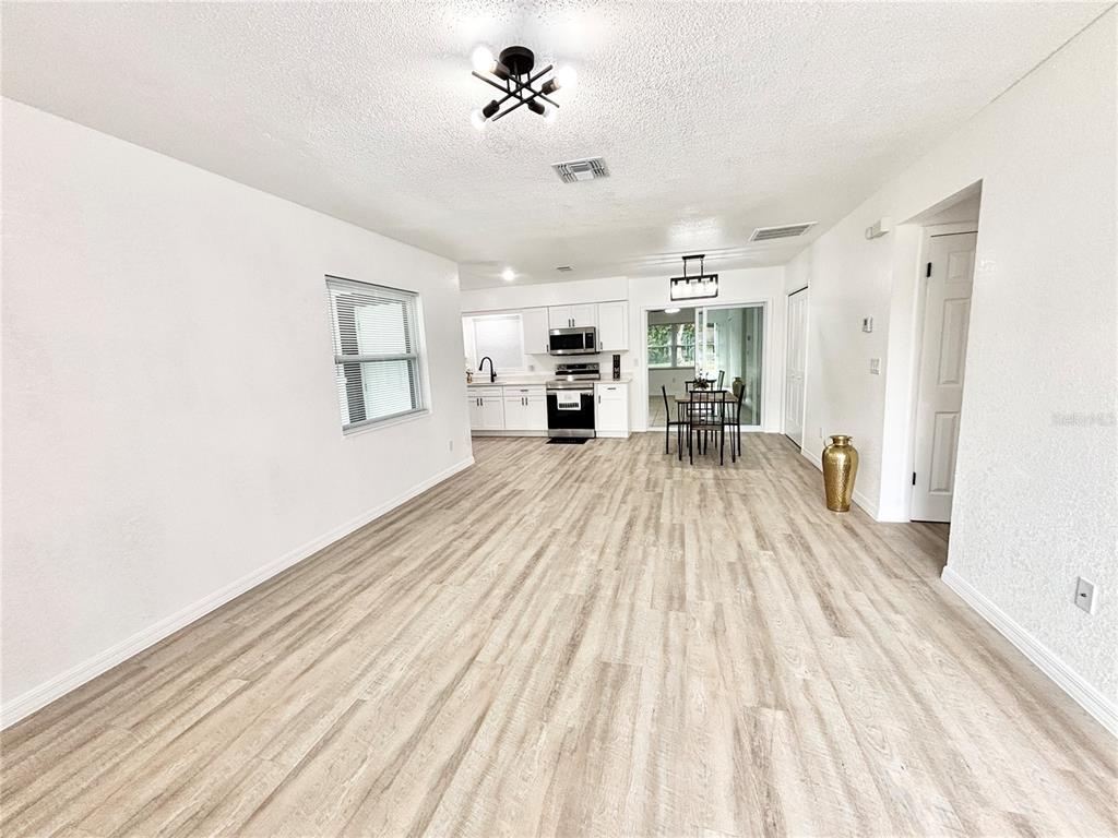 An open-concept living and dining area features light wood-look flooring and a white kitchen — 1516 AVENUE D NE, WINTER HAVEN, FL